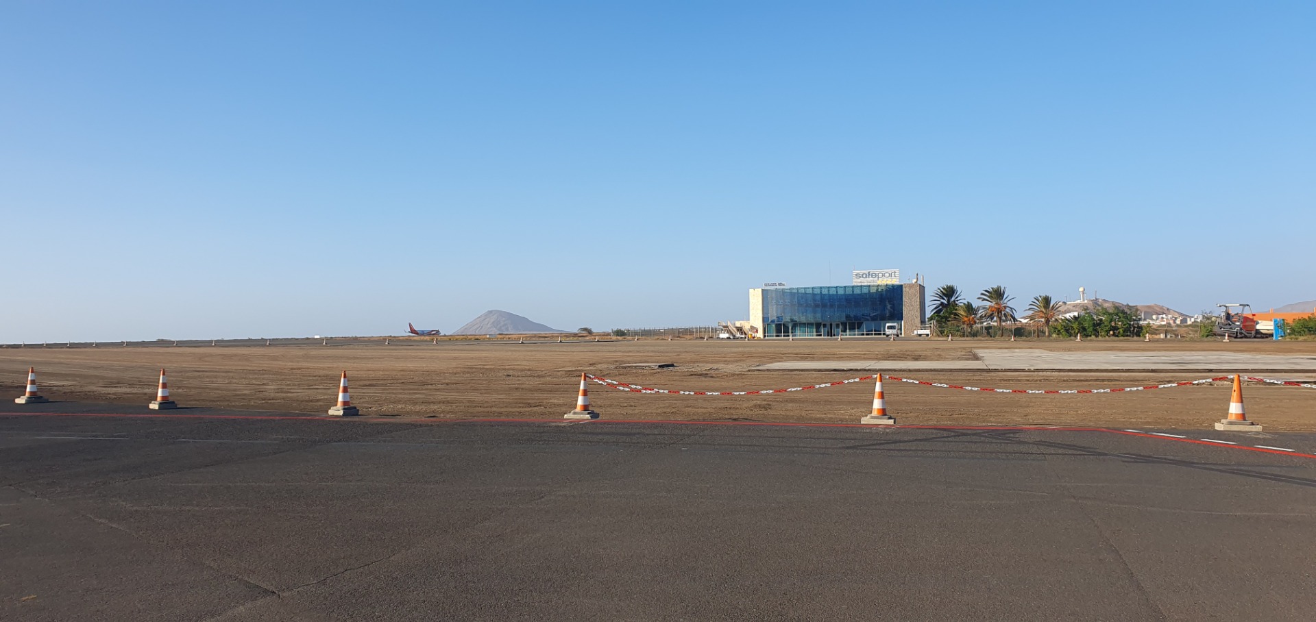 Airport runway with orange cones and red rope, Safiport building and palm trees under clear blue sky.