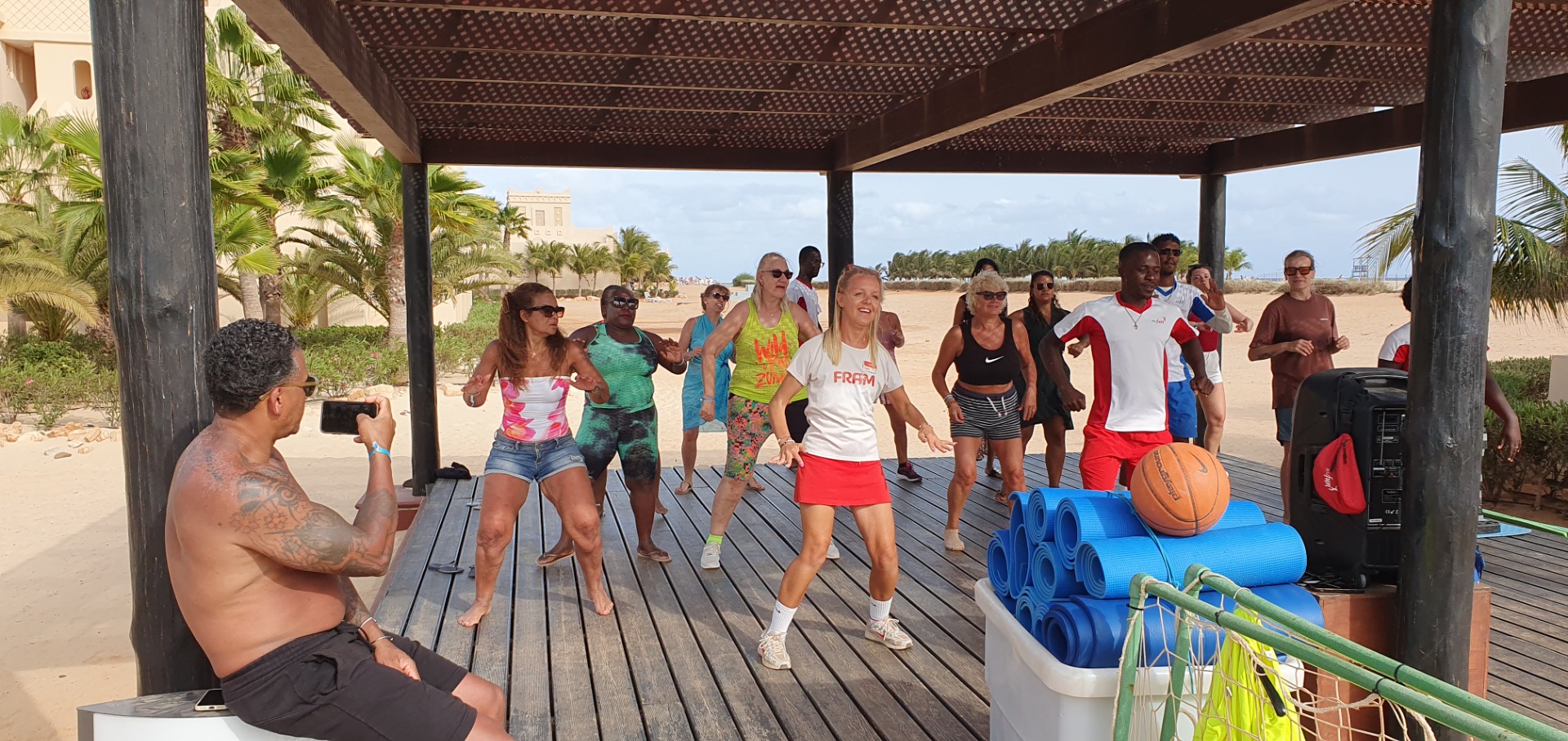 Group of people jogging on a wooden deck at beach, with yoga mats and equipment nearby.
