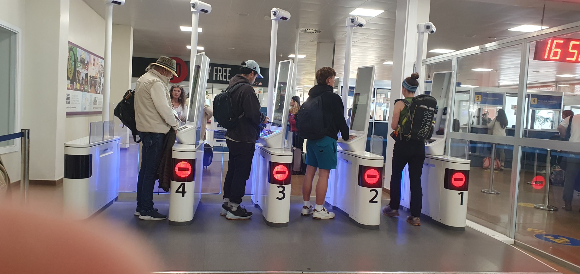 Menschen stehen an mehreren Sicherheitskontrollschleusen mit roten Anzeigen in einem Flughafen-Terminal. - EASE-Registrierung Einreise Kapverde