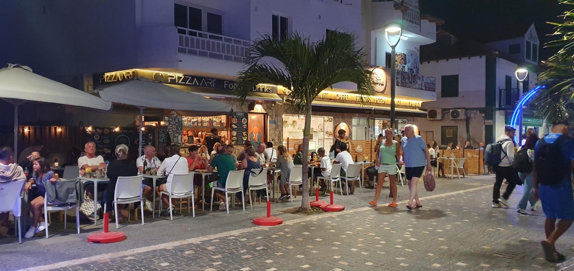 Santa Maria - Sal - Abendliche Straßenszene mit Menschen vor Pizzeria, beleuchteten Schirmen und Tischen auf gepflastertem Platz.