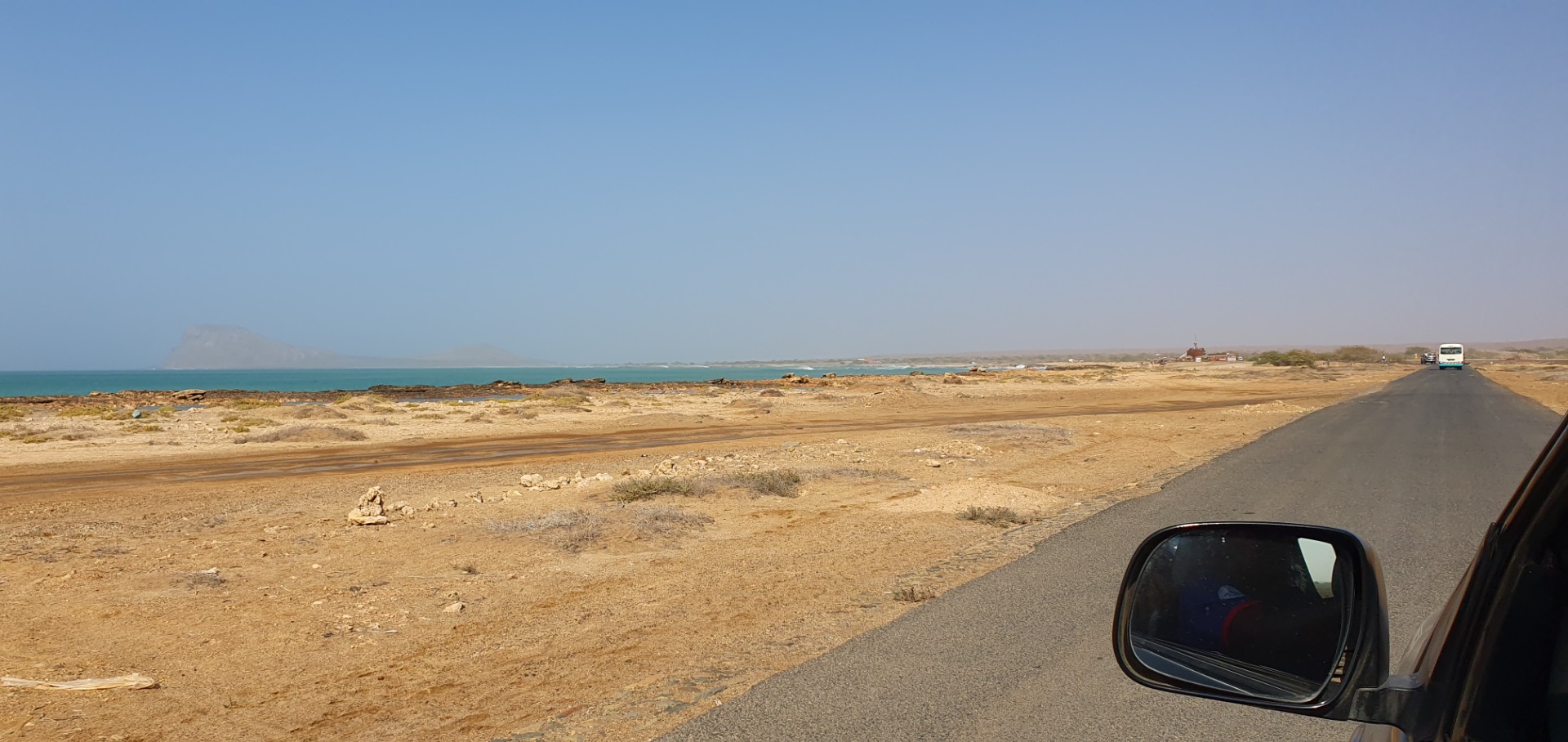 Straße am Meer in der Wüste, Blick aus dem Auto, Küste und Fahrzeuge in der Ferne.