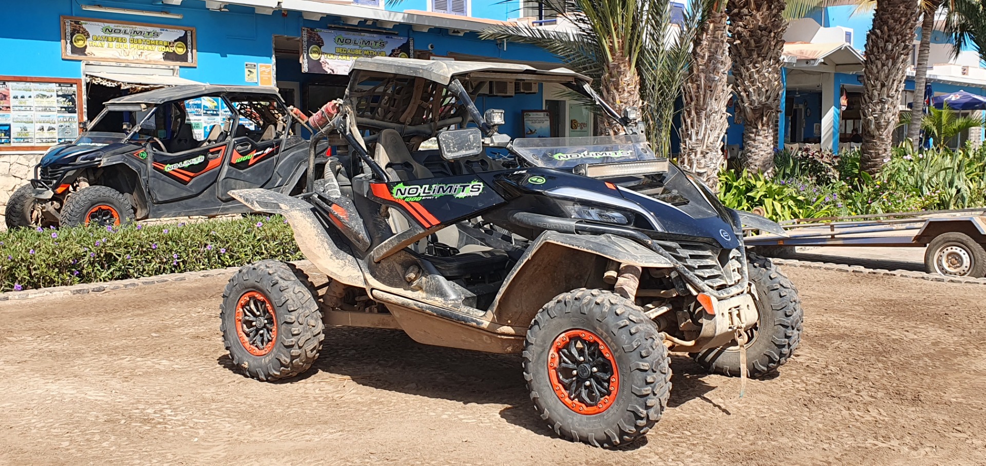 Santa Maria - Sal- Zwei Offroad-ATVs mit großen Reifen und orange-schwarzen Felgen vor blauem Gebäude, Palmen im Hintergrund.