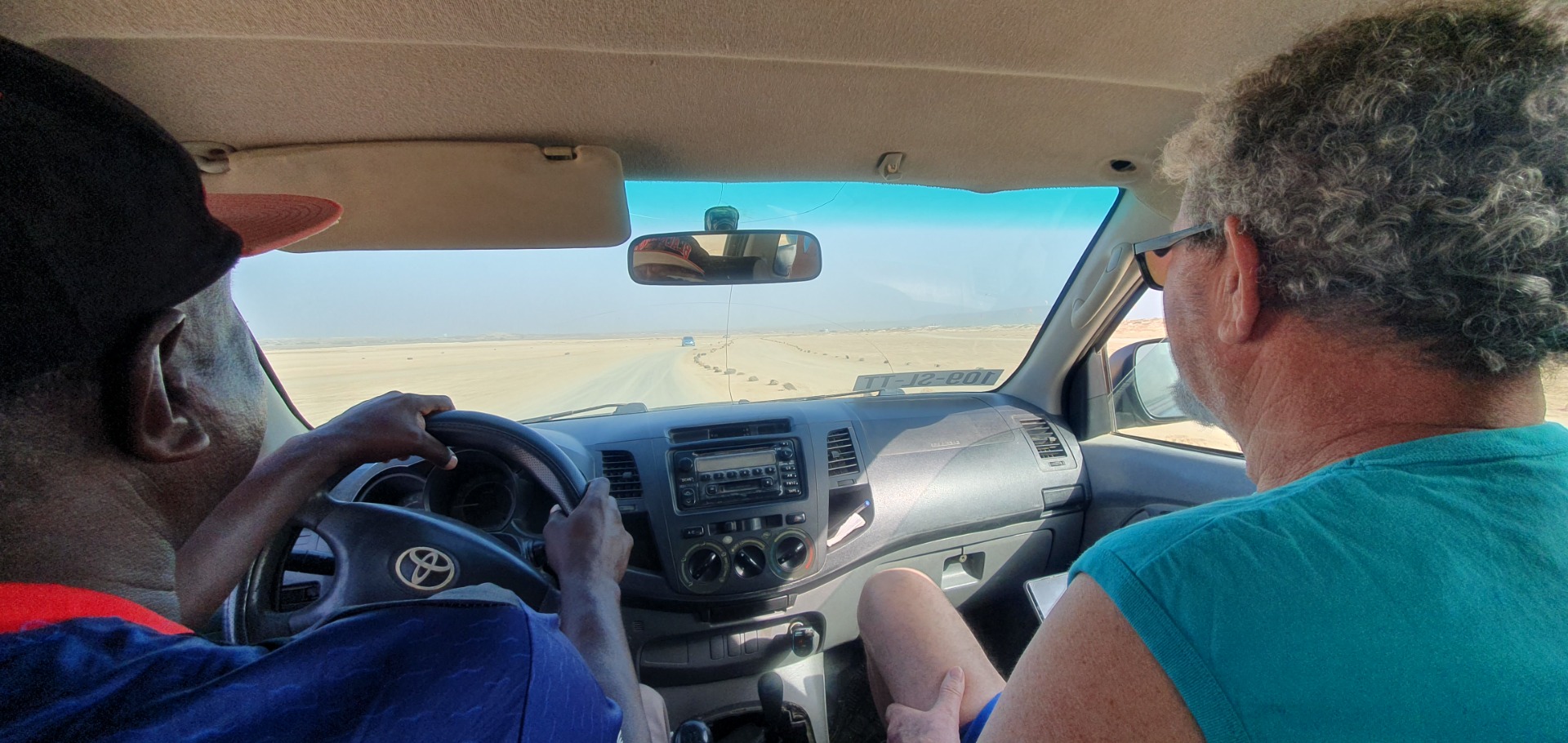 Zwei Männer fahren im Toyota durch die Wüste, Blick nach vorn aus dem Auto, Straße im Sand.