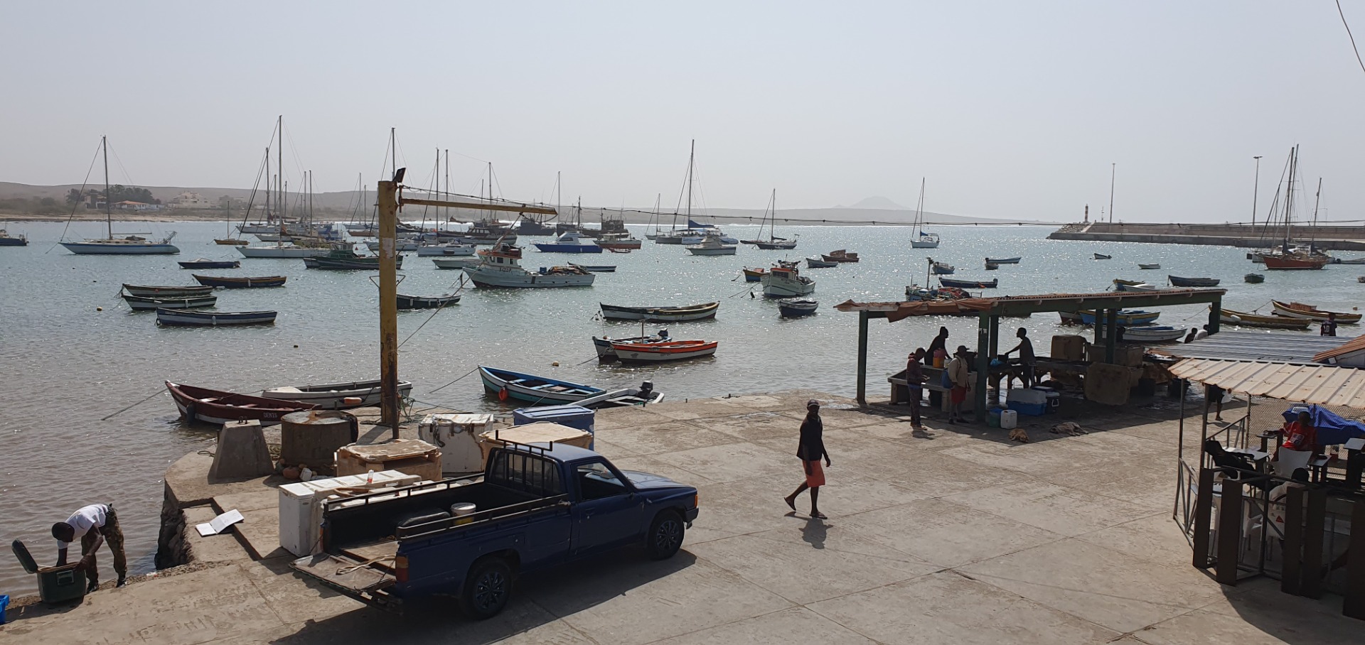 Palmeira auf Sal- der Hafen mit vielen Segelbooten, Steg, geparktem Pickup und Menschen bei bewölktem Himmel am Ufer.