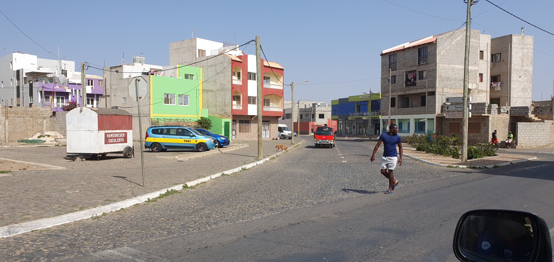 Espargos - sal -Straßenszene in einer Stadt mit bunten Gebäuden, Taxis, Autos und einem Fußgänger auf Kopfsteinpflaster.